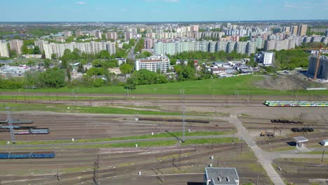 Scenic-Aerial-Shot-of-Passenger-Train-driving-into-Sunset-on-Train-Tracks-surrounded-by-Trees-above-Cityscape-forward