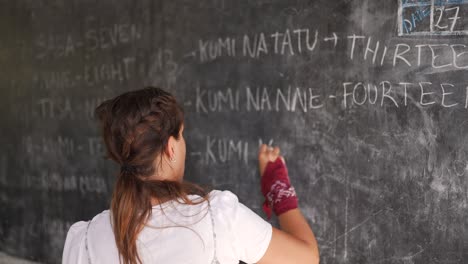 white caucasian teacher writing on the blackboard numbers teaching black african children