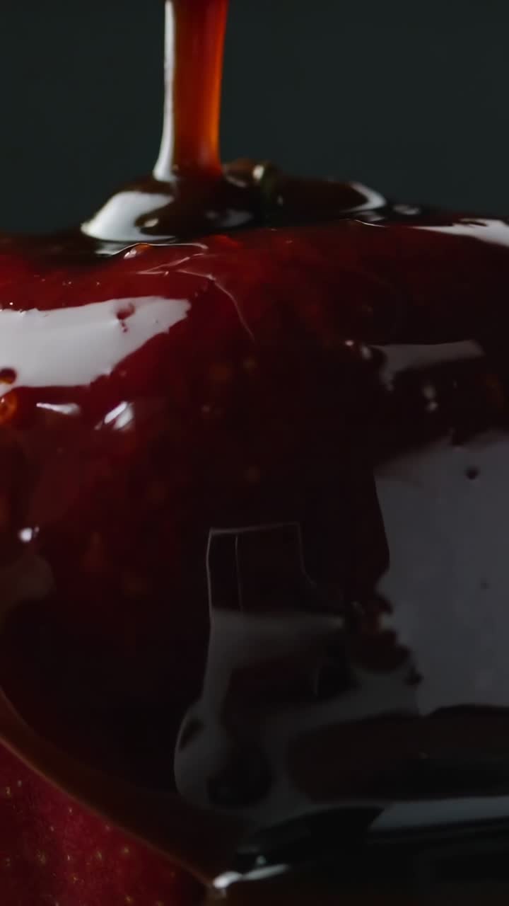 Video verticale: Flusso sottile di cioccolato fondente che cola dall'alto, ricoprendo una mela rossa in un set da studio.