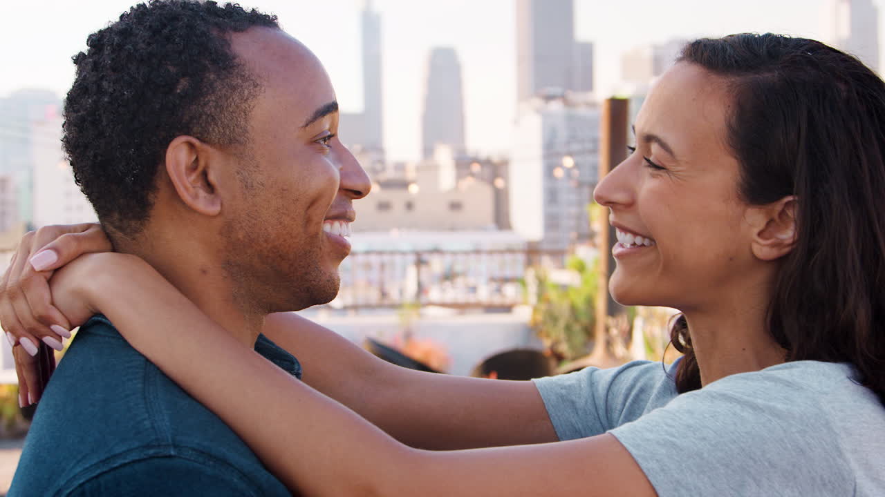 Romantic Couple Hugging On Rooftop Terrace With City Skyline In Background