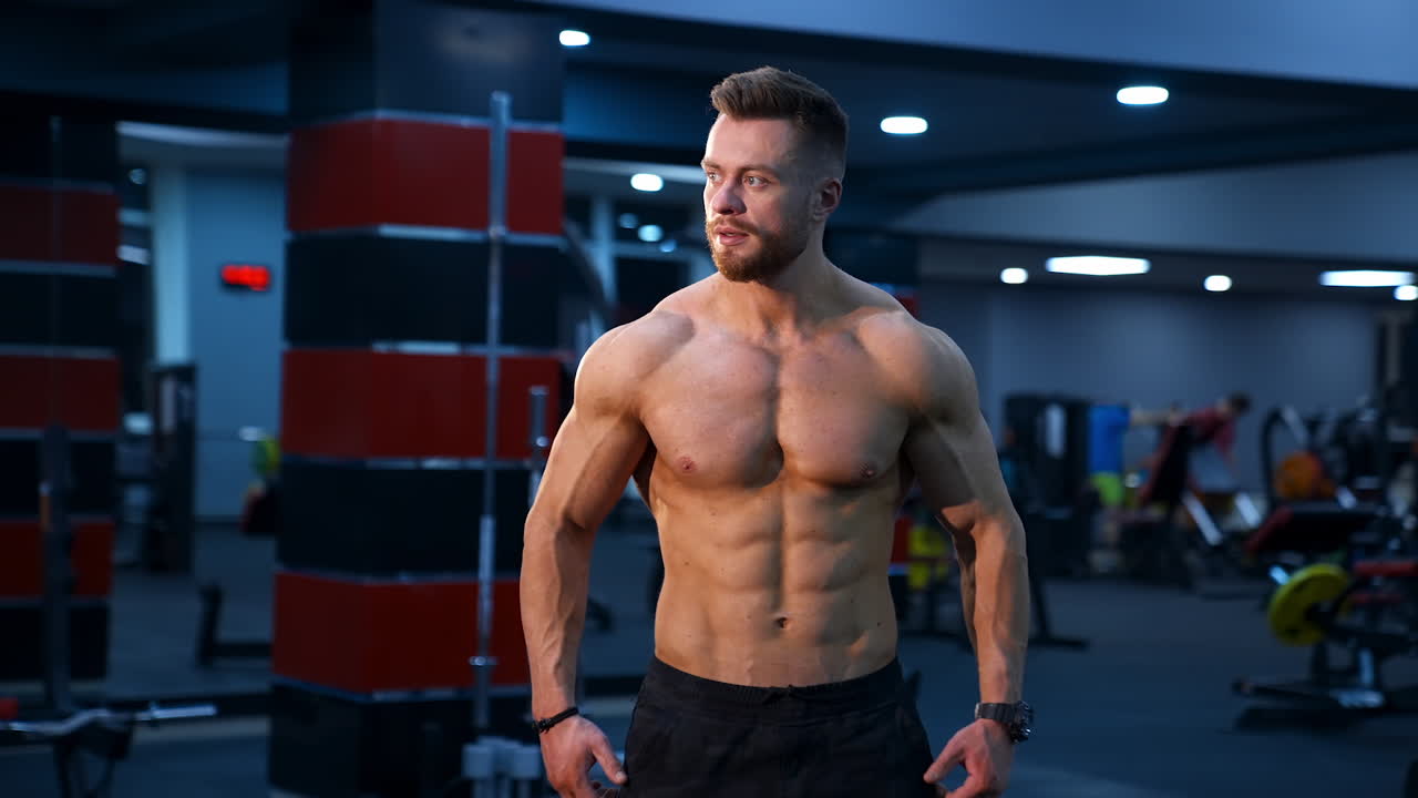 Muscle athlete strongman pumps muscules in a gym after heavy training. Perfect torso with strong abs. Handsome power male with naked torso.