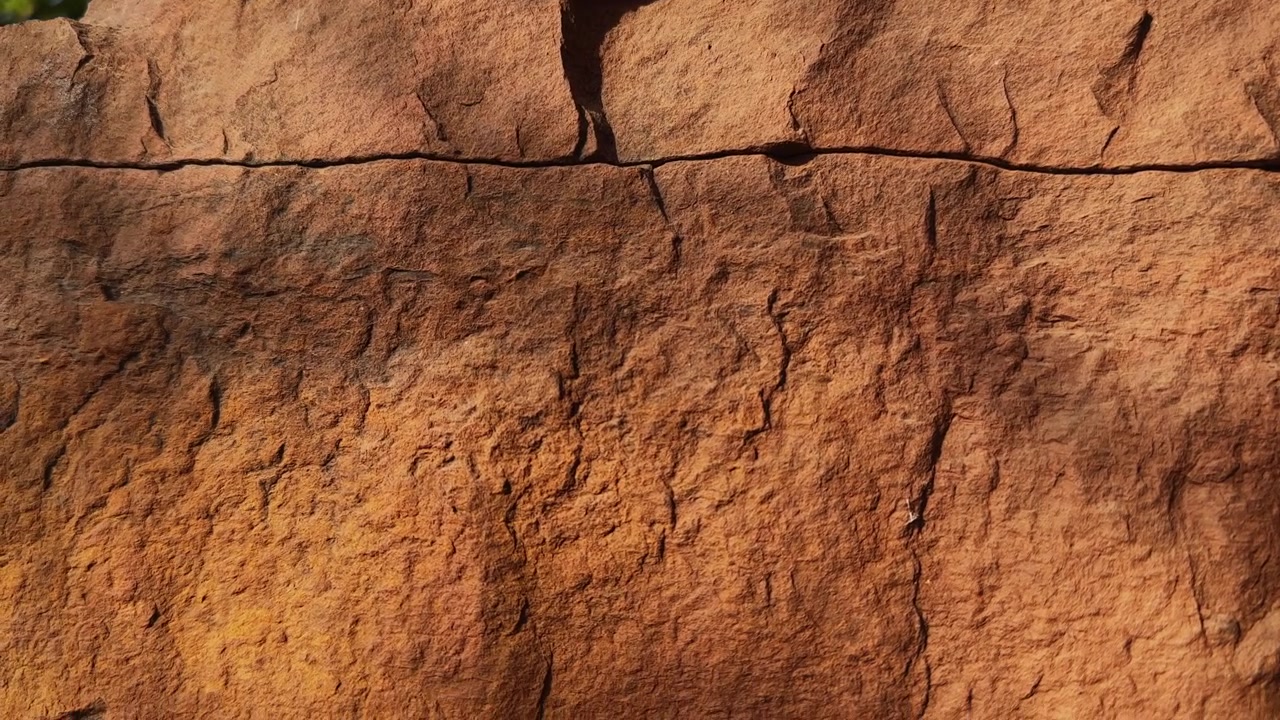 Lento movimento di discesa del braccio che rivela superfici di arenaria erose, caratterizzate da crepe naturali, modelli di erosione e texture geologiche aspre su una parete rocciosa esposta.