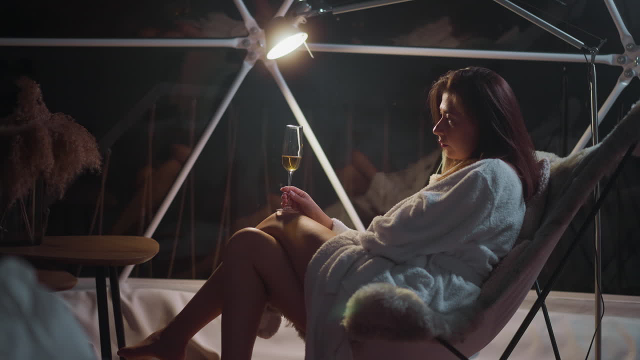 지친 여인이 손에 포도주 잔을 들고 의자에 앉아 휴가 중 외로움에 시달리고 있습니다.