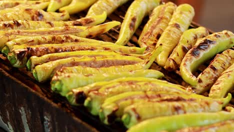 A detailed view of green chilies being grilled over an open flame, showcasing charred textures and vibrant colors.
