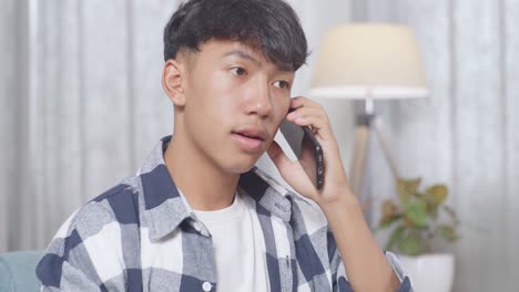 close up of asian teen boy talking on smartphone while sitting on sofa in the living room at home