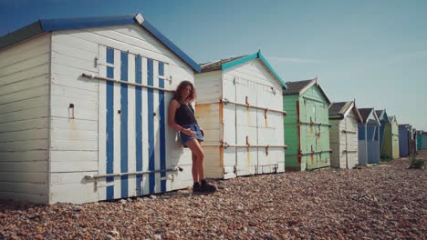 Cinemagraph---seamless-video-loop-of-a-young-brunette-woman-model-in-a-short-skirt-leaning-against-colorful-beach-huts-at-a-beach-in-Brighton,-South-England,-with-her-hair-moving-gently-in-the-wind