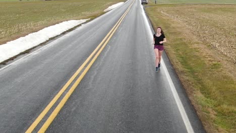 aerial tracking slow motion of teenage girl running on country road in winter