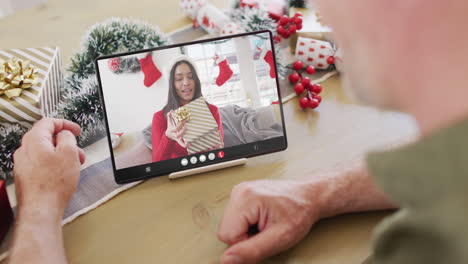hombre caucásico con decoraciones navideñas teniendo una llamada de video de tableta con una mujer biracial
