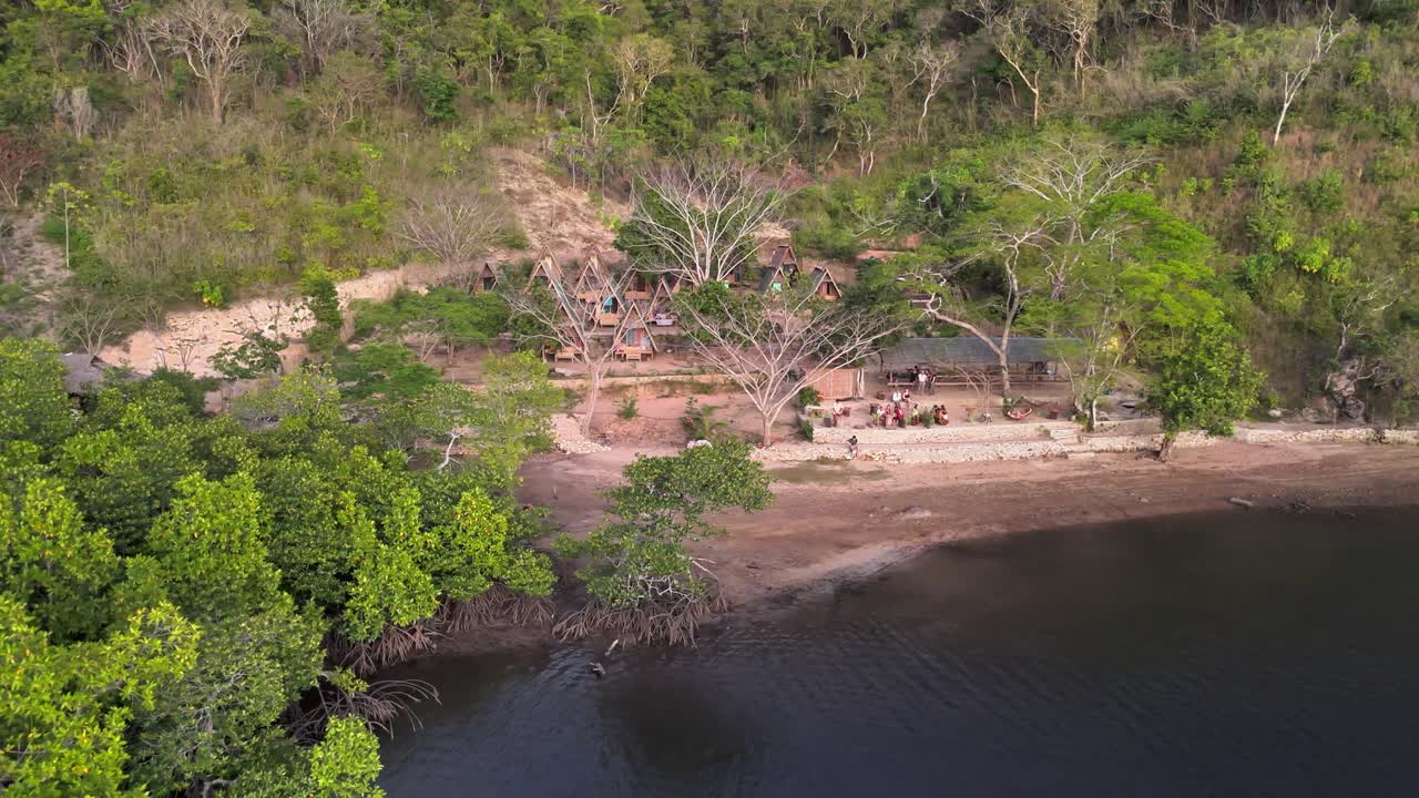 Eco-style huts nestled along the forested hillside of Sitio Coring by the water's edge in Western Culion Island, Philippines, with a serene beachfront and vibrant green surroundings