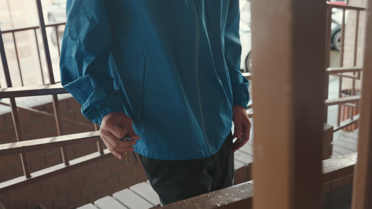 uomo con giacca blu che fuma su un balcone bagnato, pendolare pensieroso appoggiato a una ringhiera di metallo con la brace della sigaretta accesa, gocce di pioggia sulla giacca e sui gradini, strada cittadina sullo sfondo dai toni spenti, atmosfera cinematografica