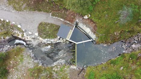 birdseye view of a small water intake to river base hydroelectric powerplant at markaani plant in vaksdal norway - top down view from intake to water pipe high up in the mountains