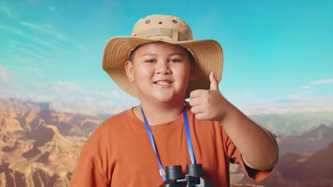 asian boy with a hat and binoculars showing magnifying glass and thumbs up gesture to camera. boy researcher examines something while traveling at the top of mountain, travel adventure, close up