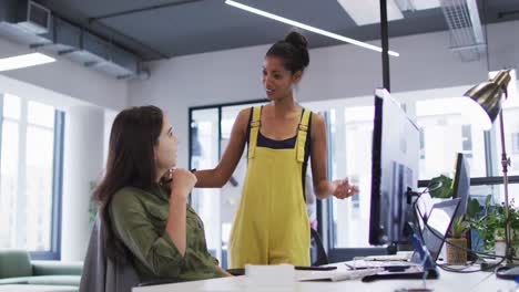 Two-diverse-female-work-colleagues-looking-at-computer-monitor-and-talking