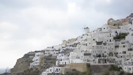 La-Icónica-Ciudad-De-Oia-En-Santorini,-Grecia,-Con-Sus-Molinos-De-Viento-Y-Sus-Impresionantes-Edificios-Blancos-A-Lo-Largo-De-La-Caldera