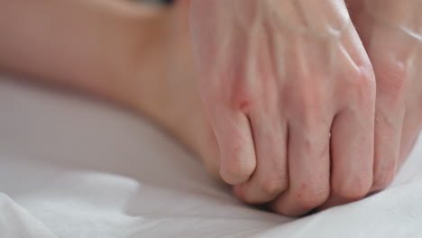 close-up view of massage therapist gently pressing client toe with both thumbs during relaxing therapy session, focusing on detailed hand movement and skin contact on soft massage surface