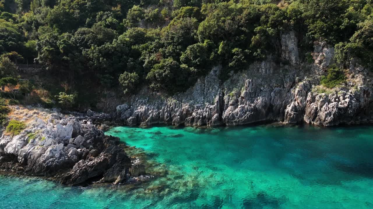 Vista aerea con drone di una baia nascosta sulla Riviera albanese con acqua turchese, scogliere e verdi colline. Tranquillo paesaggio costiero estivo, ideale per progetti di viaggio e naturalistici