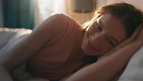 chica sonriente acostada en la cama a la luz del sol en primer plano. mujer feliz y tranquila sosteniendo una caja de regalos