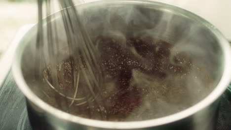 closeup of hot chocolate stirring in metal plate with whisk in slow motion.