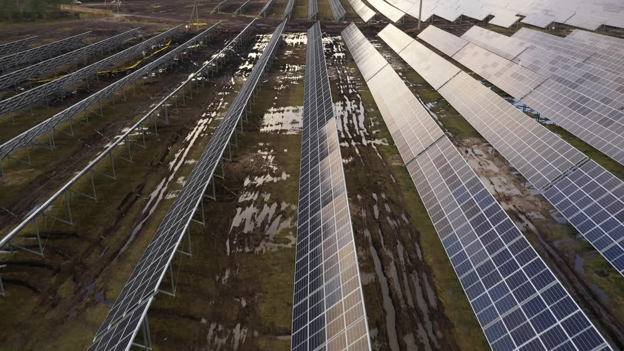 flying over in construction solar power plant, there are muddy tracks between solar panels
