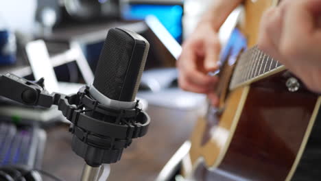 un músico de estudio tocando una guitarra acústica y grabando audio en un daw usando un micrófono de condensador
