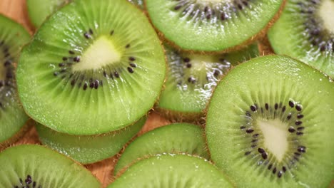 A close-up of fresh kiwi slices arranged on a wooden surface. The vibrant green color, black seeds, and juicy texture create a visually appealing composition.