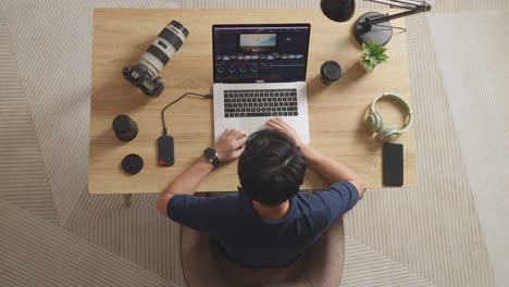 top view of asian male color grading yawning and sleeping while sitting in the workspace using a laptop next to the camera editing the video at home