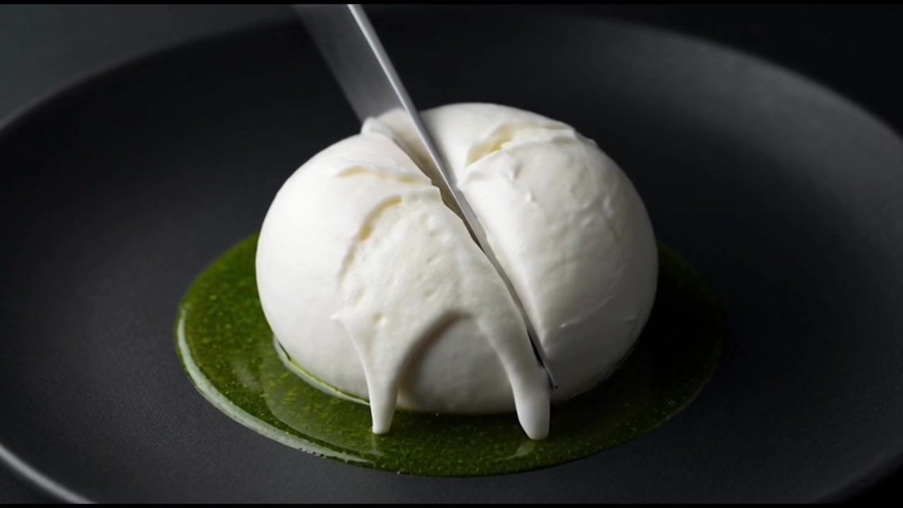 Coltello che taglia una burrata fresca su un piatto nero