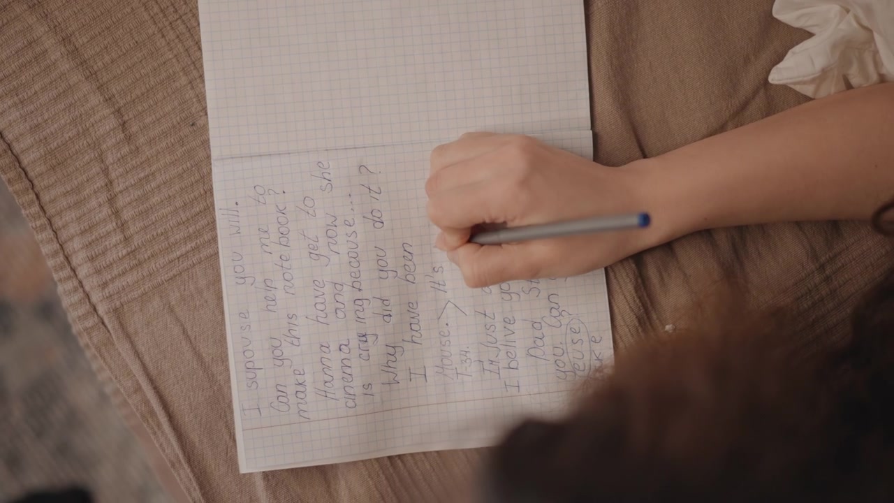 Pravá ruka drží pero nad perforovaným bílým papírem na texturované béžové dece, vytváří stabilní tečky a krátké tahy v záměrném gestu psaní deníku s měkkým neutrálním světlem a teplým detailem.
