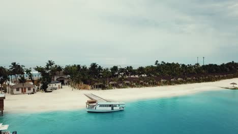 Drone-video-of-a-tropical-resort-in-the-Maldives,-blue-lagoon,-sunny-weather,-turquoise-shallow-water,-white-boat,,-island-port,-4K