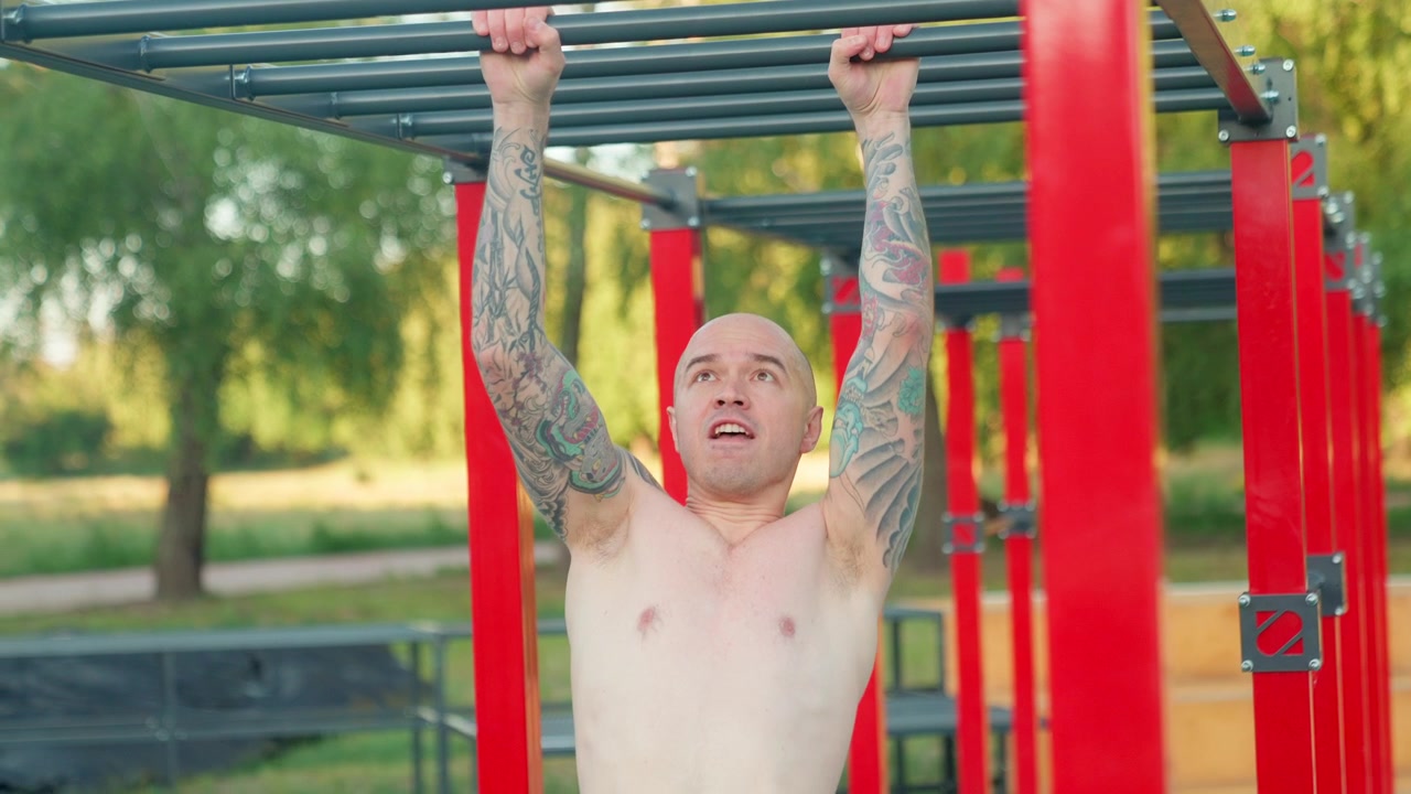 Tatoveret mand kæmper på abestigen i et udendørs fitnesscenter