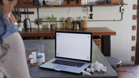 Biracial-woman-with-cold-making-video-call-using-laptop-with-copy-space-at-home,-slow-motion