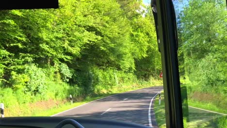 passangers point of view sitting in a bus and looking forward through a green forest in luxembourg