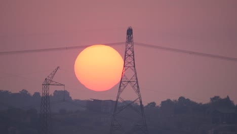 amanecer naranja con pleno sol detrás de los postes y cables eléctricos de alto voltaje