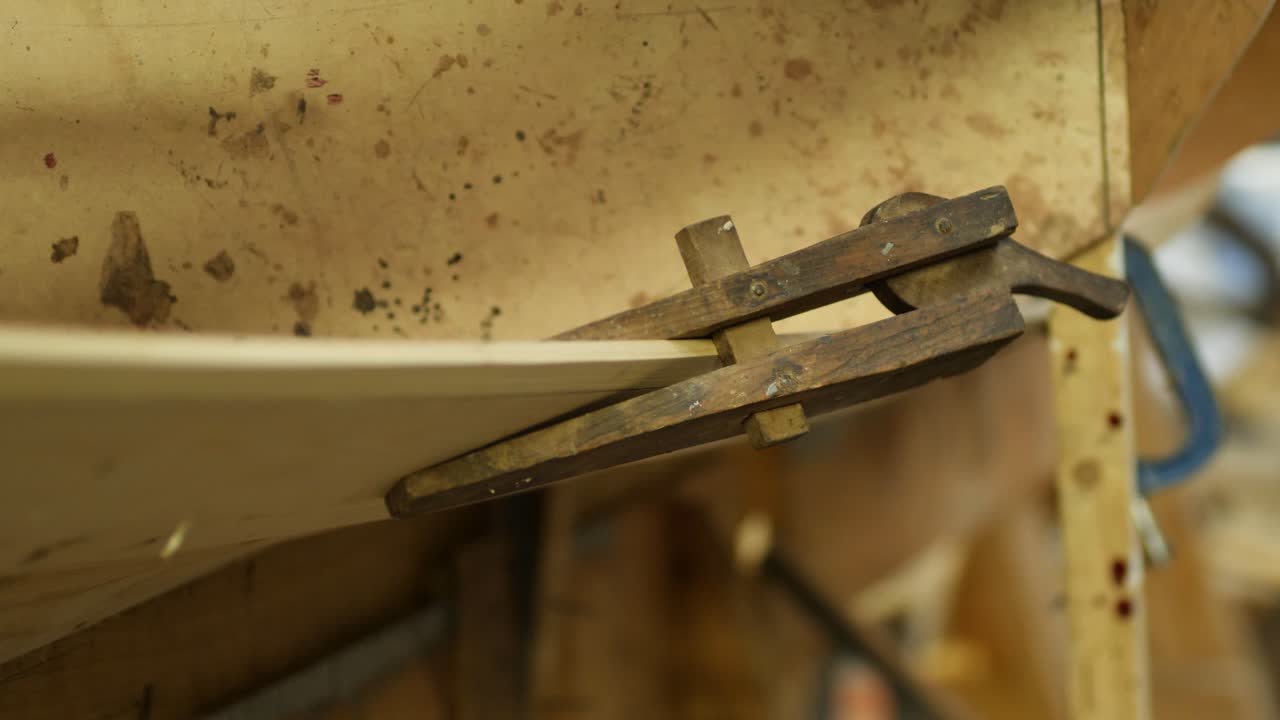 Close-up of craftsmanship restoring a clinker boat with a wooden clamp, showcasing dedication to maritime artistry. The footage highlights precision in traditional woodworking techniques.
