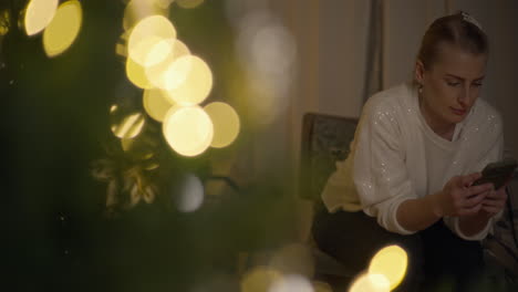 mujer usando el teléfono cerca del árbol de navidad