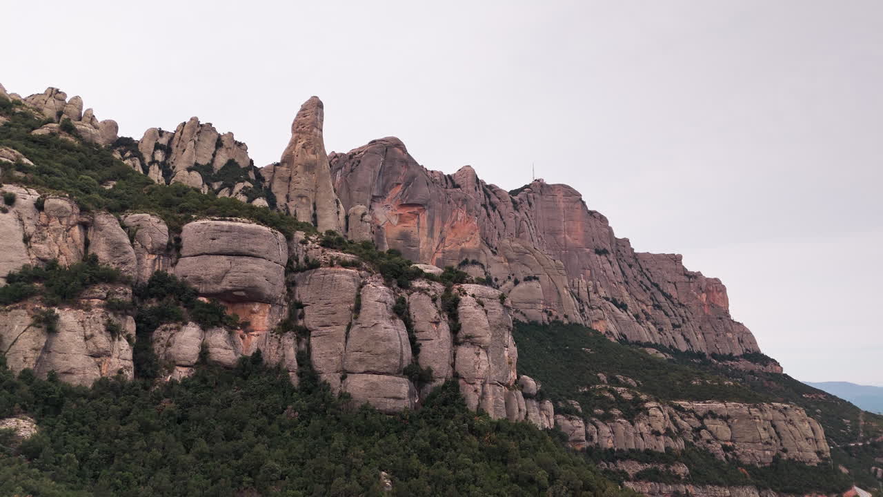 드론 크레인 다운 은 조용한 흐린 날을 배경으로 몬세라트의 둥근 절벽 꼭대기를 우아하게 드러니다.