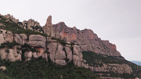 drone crane-down shot gracefully revealing the round cliff peaks of montserrat against the backdrop of a tranquil overcast day