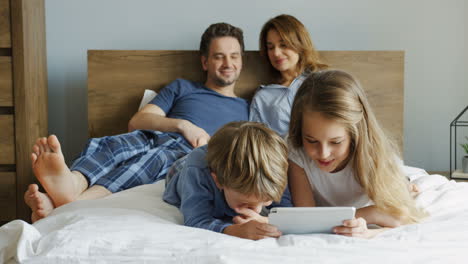 close-up view of a little girl and her brother lying on the bed and watching something on the tablet