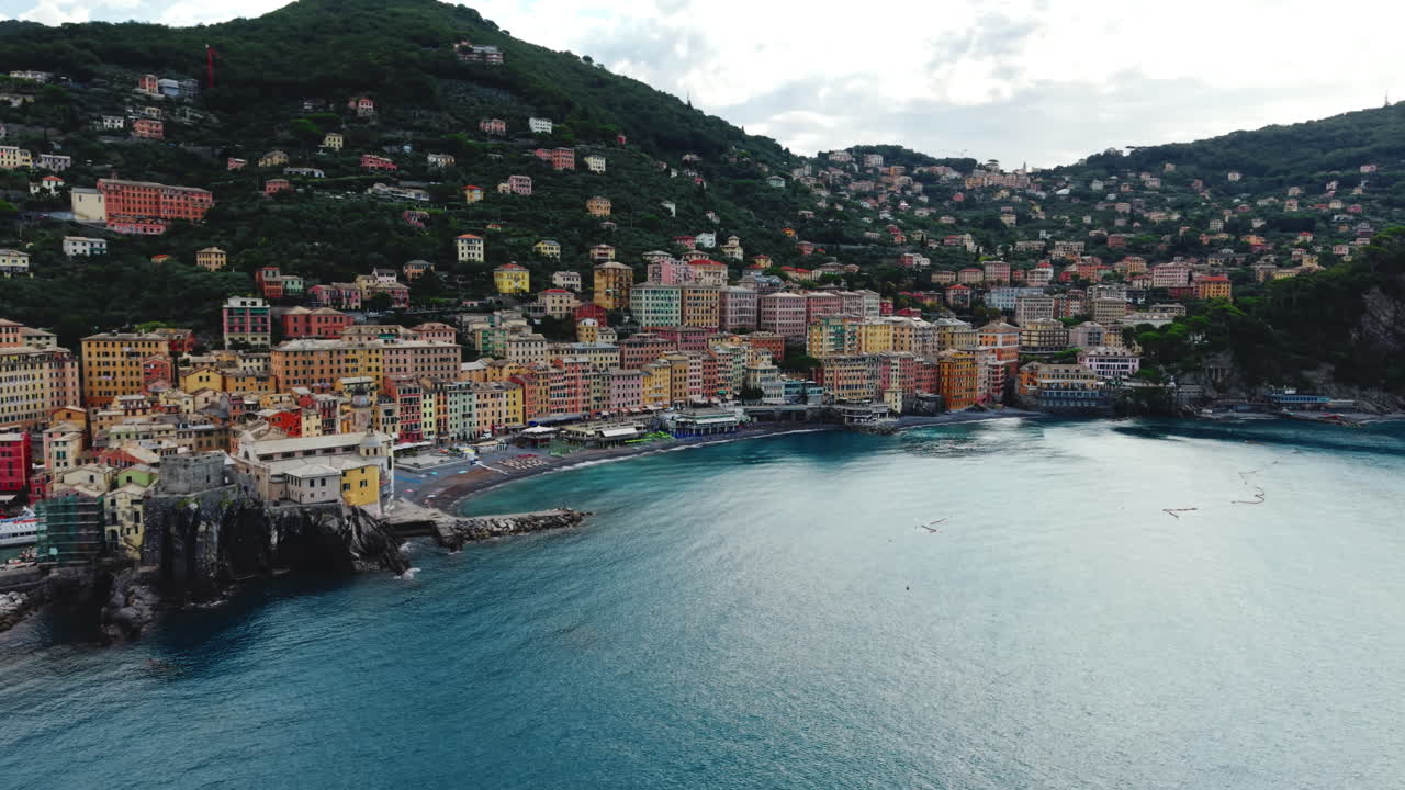 Drone si avvicina alla baia di Camogli mostrando la città, il porto e le pendici della montagna