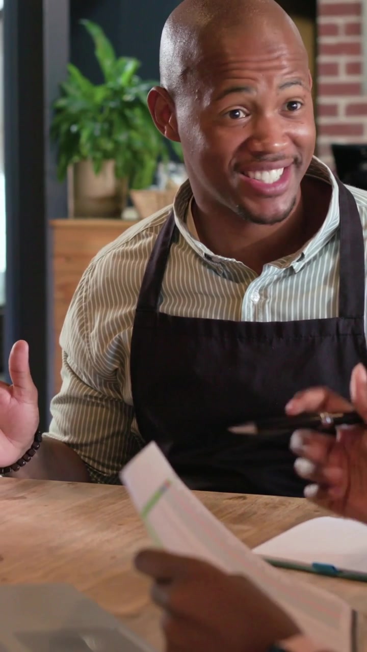 Vertical video: Camera revealing man in apron explaining documents for meeting at coffee counter