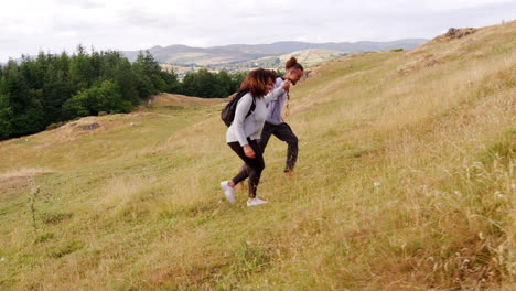 a smiling young adult couple holding hands while hiking to the summit across a field during a mountain hike