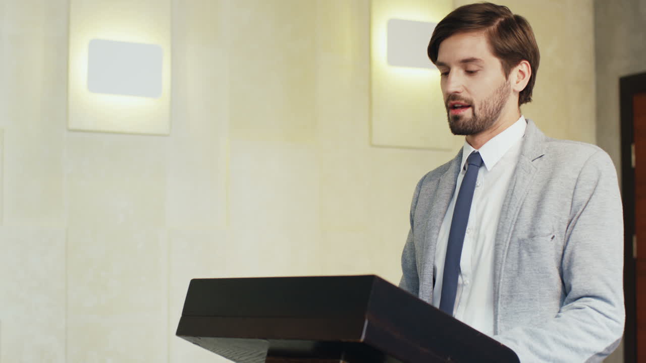 Close-up view of caucasian businessman speaker on a podium wearing formal clothes and talking in a conference room