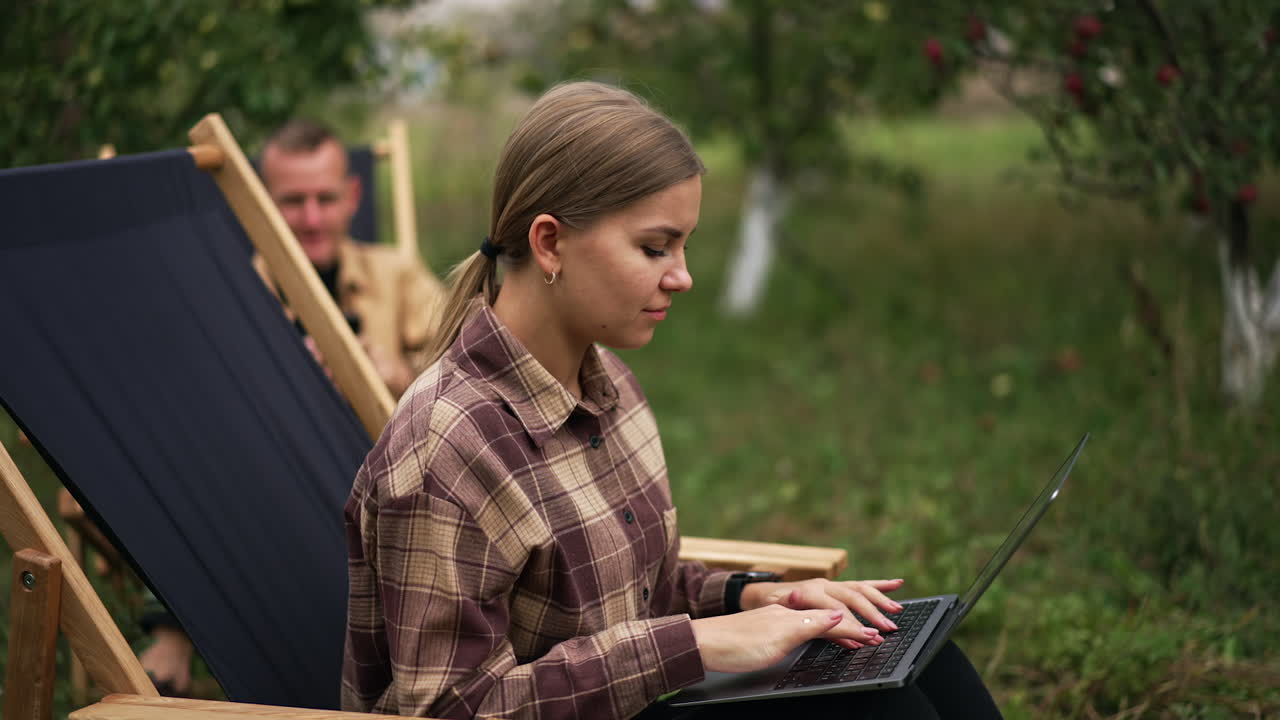 Married couple both working remotely in their garden. People feeling happy having freelance work in the comfortable place. Nature backdrop.