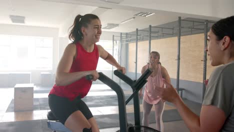 mujeres diversas sin alteración motivando a una mujer en bicicleta elíptica en clase de gimnasia grupal, en cámara lenta