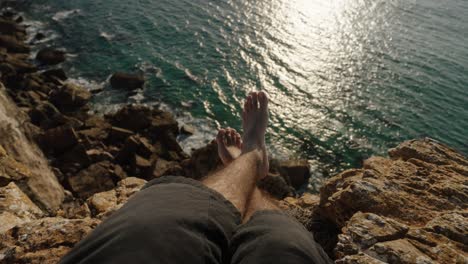 A relaxed moment with legs crossed, overlooking the sparkling ocean from a rocky cliff in Algarve, Portugal