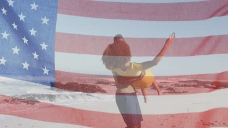 Amerikanische-Flagge-Weht-Gegen-Afroamerikanischen-Mann,-Der-Seine-Frau-Am-Strand-Abholt