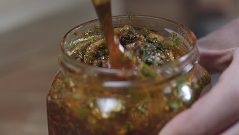 Mix-with-small-spoon,-argentine-chimichurri-ingredients-in-a-jar,-barbecue-sauce