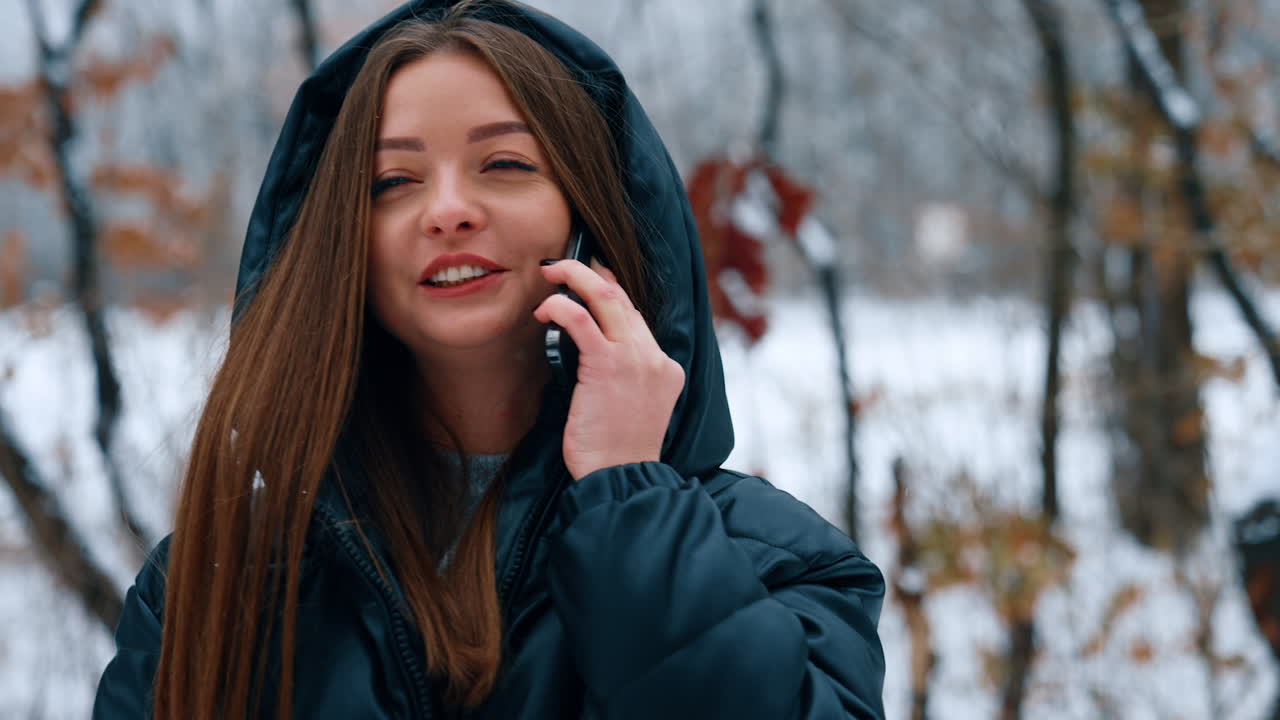 Positive cheerful Caucasian lady speaks on the phone outdoors. Woman drinks coffee walking in the winter park.