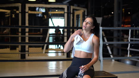 mujer descansando y bebiendo agua en un ring de boxeo en el gimnasio