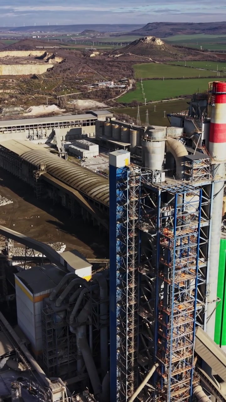 Fabbrica di cemento con macchinari e campi vicino alle colline in una giornata di sole